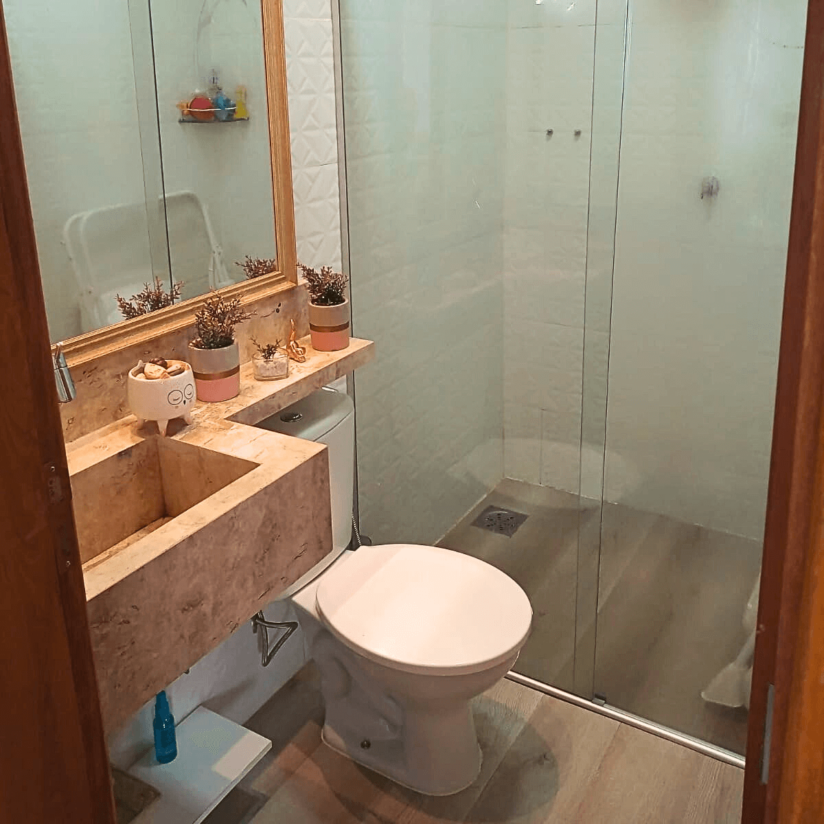 Banheiro moderno reformado com bancada em madeira rústica, cuba de sobrepor e box de vidro transparente.