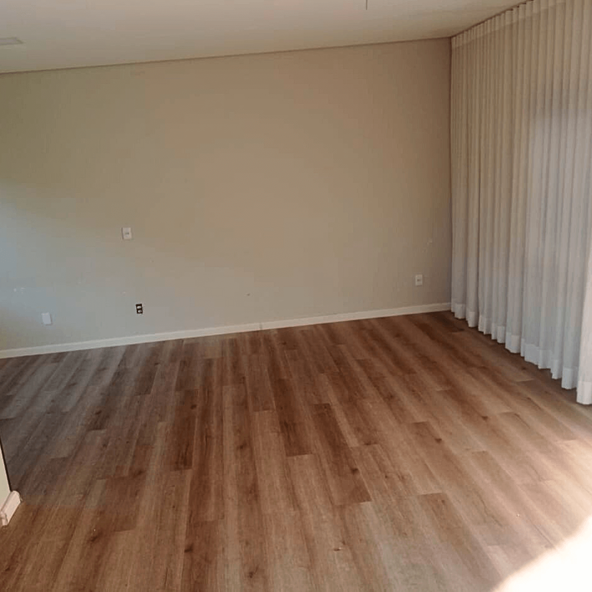 Sala residencial vazia após instalação de piso laminado cor madeira natural e rodapés brancos.